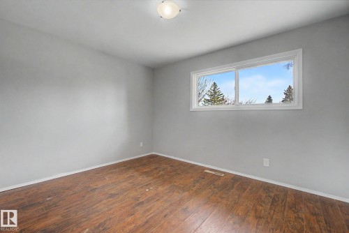 Spacious room featuring wood-finish flooring, a contemporary ceiling light fixture, and a large window with white trim - 6048 105B Street, Edmonton, AB - Indoor Photo Showing Other Room