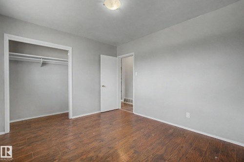 Room featuring wood-finish flooring, light gray walls, a flush-mount ceiling light, a built-in closet with shelving and hanging rods, and a white interior door - 6048 105B Street, Edmonton, AB - Indoor Photo Showing Other Room