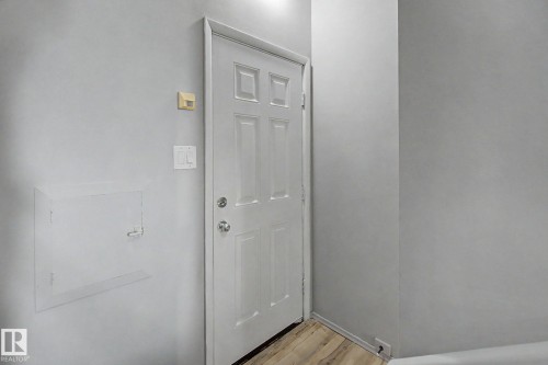 Entryway featuring a paneled door with polished hardware, light gray wall finishes, wood-finish flooring, and white baseboards - 6048 105B Street, Edmonton, AB - Indoor Photo Showing Other Room