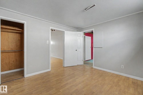 Spacious room featuring wood-finish flooring, light gray wall paint, white trim, a built-in closet with wood paneling and metal hanging rods, and two panel doors - 6048 105B Street, Edmonton, AB - Indoor Photo Showing Other Room