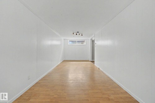 Long room featuring white paneling, light wood-finish flooring, a rectangular window, and a ceiling-mounted light fixture - 6048 105B Street, Edmonton, AB - Indoor Photo Showing Other Room