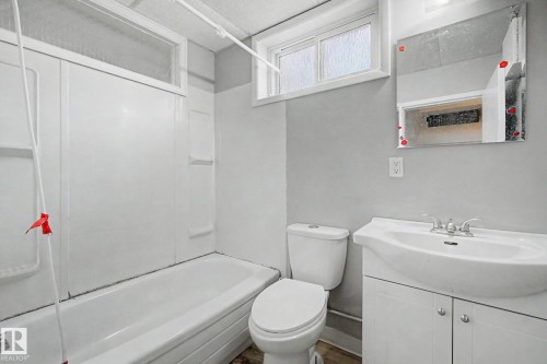 Bathroom featuring a white bathtub and shower surround, a single vanity with a white ceramic sink, a mirror, and a window with frosted glass - 6048 105B Street, Edmonton, AB - Indoor Photo Showing Bathroom