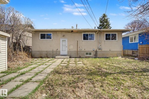 Rear exterior featuring a stucco facade, multiple windows, a white door, and a concrete paver pathway - 6048 105B Street, Edmonton, AB - Outdoor