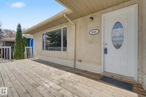 Expansive wooden deck with railing, featuring a stucco exterior and a white entry door with an oval decorative glass insert - 6048 105B Street, Edmonton, AB - Outdoor With Deck Patio Veranda With Exterior