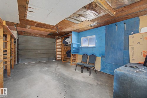 Single-car garage with a roll-up door, featuring exposed wooden ceiling beams and concrete flooring - 6048 105B Street, Edmonton, AB - Indoor Photo Showing Garage