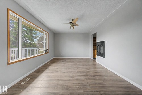 Spacious interior featuring wood-finish flooring, a large picture window with wood trim, a ceiling fan, and a built-in fireplace insert - 6048 105B Street, Edmonton, AB - Indoor Photo Showing Other Room