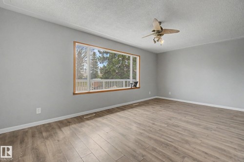 Spacious room featuring wood-finish flooring, a large window with wood trim, and a ceiling fan with integrated lighting - 6048 105B Street, Edmonton, AB - Indoor