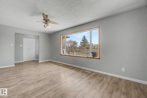 Spacious room featuring wood-finish flooring, a large picture window with wood trim, a ceiling fan with integrated lighting, and a double-door closet with white panels - 6048 105B Street, Edmonton, AB - Indoor Photo Showing Other Room