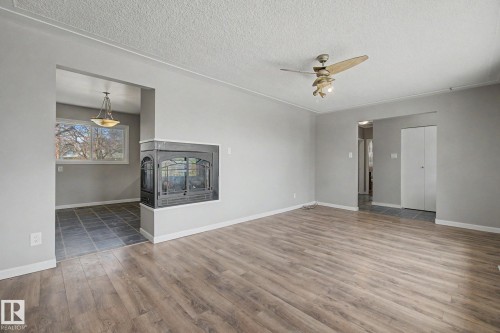 Spacious room featuring wood-finish flooring, a contemporary ceiling fan, and a built-in fireplace with a dark metal surround - 6048 105B Street, Edmonton, AB - Indoor Photo Showing Other Room