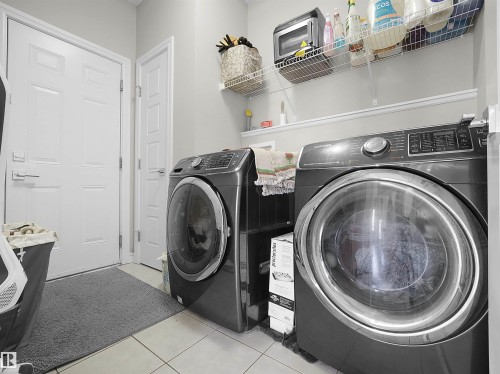 Dedicated laundry area featuring a front-loading washer and dryer, tile flooring, overhead wire shelving, and a built-in wall shelf - 3247 15 Avenue Nw, Edmonton, AB 