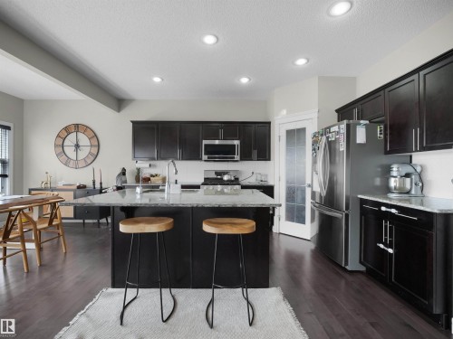 Kitchen featuring dark wood-finish cabinetry, light-toned countertops, stainless steel appliances, a center island with sink, and wood-finish flooring - 3247 15 Avenue Nw, Edmonton, AB 