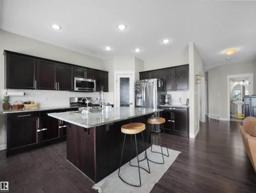 Kitchen featuring a large island with granite countertop, dark wood-finish cabinetry, stainless steel appliances, and wood-finish flooring - 3247 15 Avenue Nw, Edmonton, AB 
