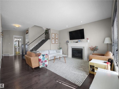 Spacious living area featuring dark wood-finish flooring, a white mantel fireplace, and a staircase with dark wood railings - 3247 15 Avenue Nw, Edmonton, AB 