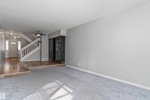 Spacious living area featuring light gray wall paint, light gray carpeting, and white baseboards - 6734 36A Avenue, Edmonton, AB 