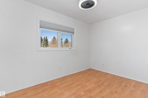 Room featuring wood-finish flooring, a double-pane window with white blinds, and a flush-mount ceiling light fixture - 6734 36A Avenue, Edmonton, AB 