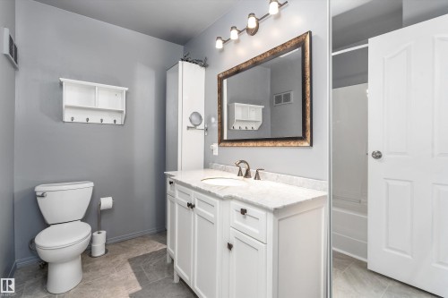 Bathroom featuring a white vanity with a stone-finish countertop, undermount sink, and bronze-finish faucet - 6734 36A Avenue, Edmonton, AB 