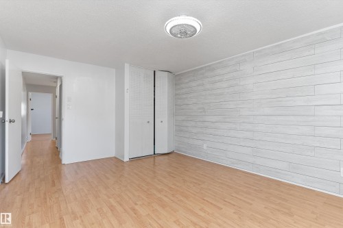 Interior room featuring a prominent accent wall with horizontal paneling, wood-finish flooring, a ceiling-mounted light fixture, and white bi-fold closet doors - 6734 36A Avenue, Edmonton, AB 