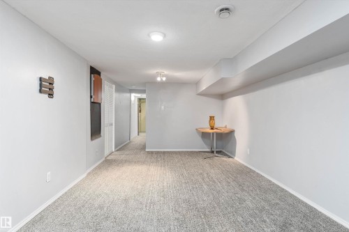 Spacious room featuring textured gray carpeting, white baseboards, and light gray painted walls - 6734 36A Avenue, Edmonton, AB 