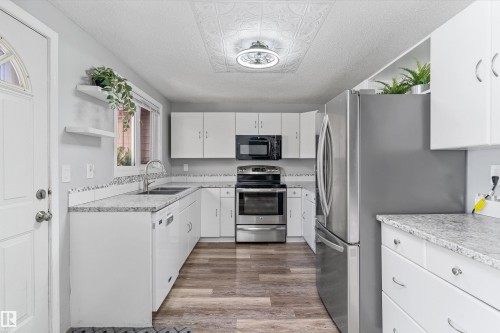 Kitchen featuring wood-finish flooring, white cabinetry, speckled countertops, stainless steel appliances, and a decorative ceiling panel - 6734 36A Avenue, Edmonton, AB 