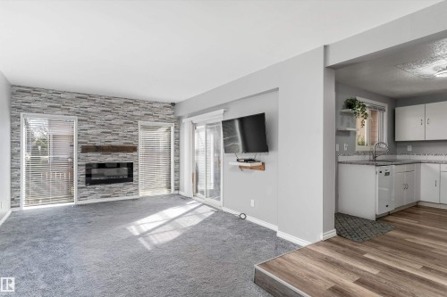 Living area featuring a textured stone-look accent wall with an electric fireplace, a wood mantel, and two vertical windows with blinds - 6734 36A Avenue, Edmonton, AB 