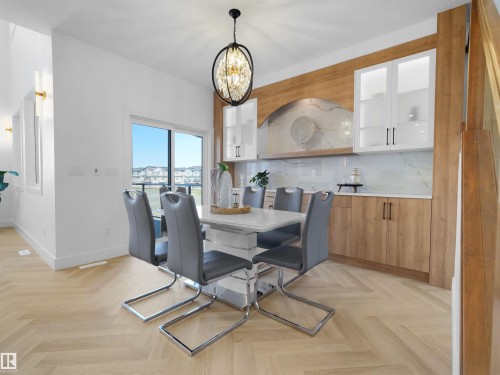 Herringbone wood-finish flooring provides a striking foundation for this bright dining area, featuring a contemporary chandelier - 209 Crystal Creek Dr Nw, Leduc, AB - Indoor Photo Showing Dining Room