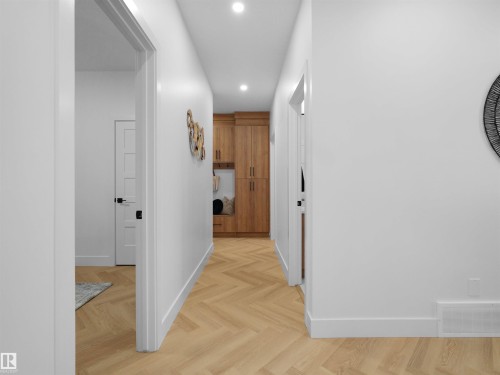 Hallway featuring wood-finish herringbone flooring, recessed lighting, white walls, and a built-in wood-finish storage unit - 209 Crystal Creek Dr Nw, Leduc, AB - Indoor Photo Showing Other Room