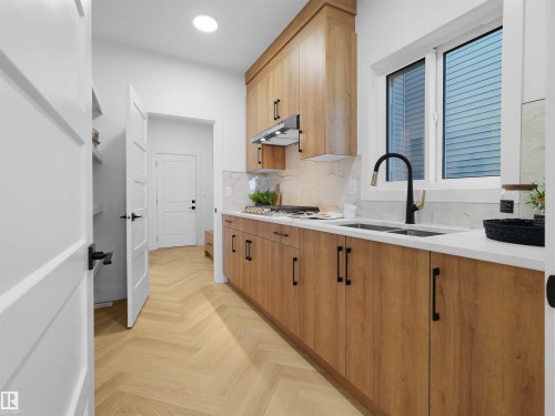 Modern kitchen featuring wood-finish cabinetry with black hardware, white countertops, and a full tile backsplash - 209 Crystal Creek Dr Nw, Leduc, AB - Indoor Photo Showing Kitchen With Double Sink