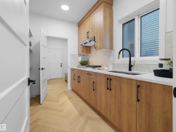 Modern kitchen featuring wood-finish cabinetry with black hardware, white countertops, and a full tile backsplash - 