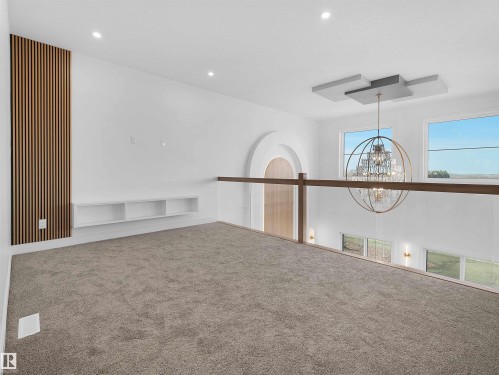 Carpeted loft area featuring a wood slat accent wall, recessed lighting, built-in shelving, and an open railing overlooking a lower space with a prominent chandelier - 209 Crystal Creek Dr Nw, Leduc, AB - Indoor Photo Showing Other Room