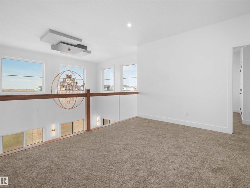 Open loft area featuring neutral-toned carpet, a modern chandelier with a unique ceiling mount, and multiple windows providing ambient light - 209 Crystal Creek Dr Nw, Leduc, AB - Indoor Photo Showing Other Room