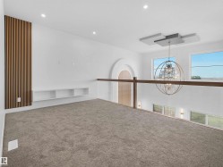Carpeted loft area featuring a wood slat accent wall, recessed lighting, built-in shelving, and an open railing overlooking a lower space with a prominent chandelier - 