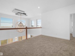 Open loft area featuring neutral-toned carpet, a modern chandelier with a unique ceiling mount, and multiple windows providing ambient light - 