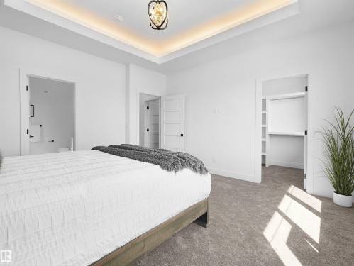 Carpeted bedroom featuring a tray ceiling with cove lighting and a decorative chandelier - 209 Crystal Creek Dr Nw, Leduc, AB - Indoor Photo Showing Bedroom