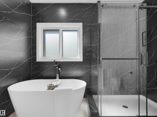 Freestanding soaking tub complemented by striking black marble-look wall tiling - 209 Crystal Creek Dr Nw, Leduc, AB - Indoor Photo Showing Bathroom