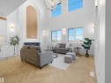 Vaulted ceilings with an elegant chandelier, a prominent fireplace with an arched wood-finish accent, herringbone wood-finish flooring, and multiple windows providing ambient light - 209 Crystal Creek Dr Nw, Leduc, AB  - Indoor 