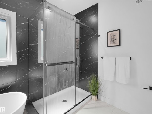 Glass-enclosed shower featuring black marble-style tile surround and a white shower pan - 209 Crystal Creek Dr Nw, Leduc, AB - Indoor Photo Showing Bathroom