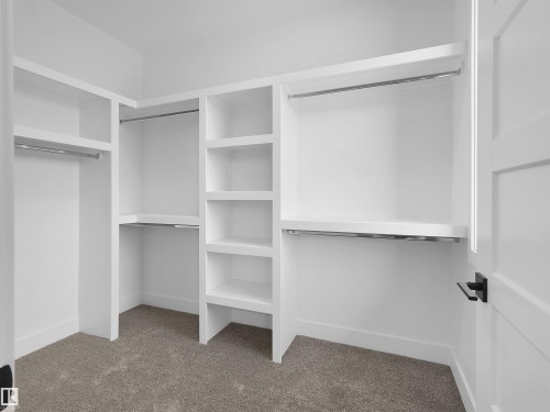 Walk-in closet featuring built-in shelving, multiple hanging rods, and neutral-toned carpeting - 209 Crystal Creek Dr Nw, Leduc, AB - Indoor With Storage