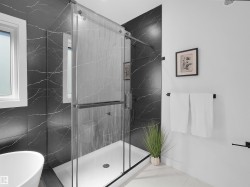 Glass-enclosed shower featuring black marble-style tile surround and a white shower pan - 