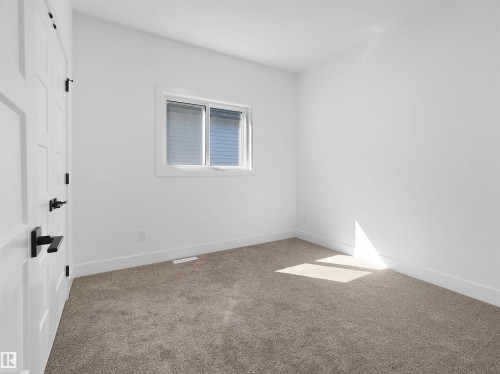 Carpeted interior room featuring a white paneled door with black hardware, white walls, and a window with white trim and blinds - 209 Crystal Creek Dr Nw, Leduc, AB - Indoor Photo Showing Other Room
