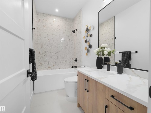 Full bathroom featuring a white soaking tub with a tiled shower surround, a light wood-finish vanity with an integrated sink and white countertop, and a large wall-mounted mirror - 209 Crystal Creek Dr Nw, Leduc, AB - Indoor Photo Showing Bathroom