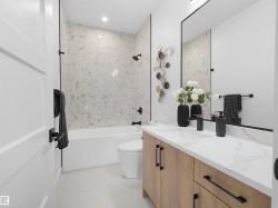 Full bathroom featuring a white soaking tub with a tiled shower surround, a light wood-finish vanity with an integrated sink and white countertop, and a large wall-mounted mirror - 
