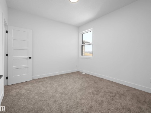 Neutral-toned carpeting, white wall finishes, a modern four-panel door with black hardware, a flush-mount ceiling light fixture, and a white-framed window - 209 Crystal Creek Dr Nw, Leduc, AB - Indoor Photo Showing Other Room
