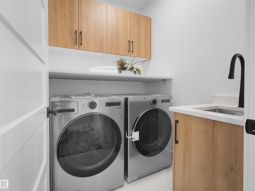 Laundry room featuring wood-finish cabinetry, white countertops, built-in shelving, and a stainless steel sink with a matte black faucet - 209 Crystal Creek Dr Nw, Leduc, AB - Indoor Photo Showing Laundry Room
