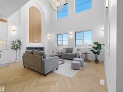 Vaulted ceilings with an elegant chandelier, a prominent fireplace with an arched wood-finish accent, herringbone wood-finish flooring, and multiple windows providing ambient light - 