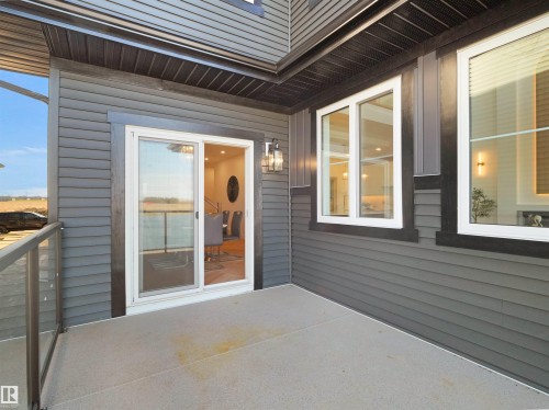 Outdoor patio with gray siding exterior, featuring a glass panel railing, sliding glass door, and multiple windows with white frames - 209 Crystal Creek Dr Nw, Leduc, AB - Outdoor With Deck Patio Veranda With Exterior