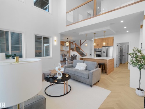 Two-story living area with high ceilings, large windows, and herringbone wood-finish flooring - 209 Crystal Creek Dr Nw, Leduc, AB - Indoor Photo Showing Living Room