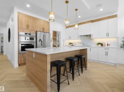 Gourmet kitchen featuring a substantial island with seating, stainless steel appliances, herringbone wood-finish flooring, white shaker cabinetry, and unique pendant lighting - 