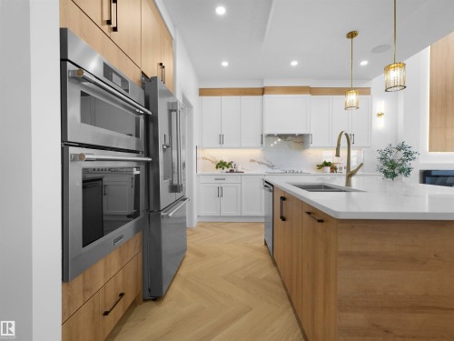 Gourmet kitchen with stainless steel appliances, herringbone wood-finish flooring, white cabinetry, a large kitchen island with a sink, and pendant lighting - 209 Crystal Creek Dr Nw, Leduc, AB - Indoor Photo Showing Kitchen With Double Sink With Upgraded Kitchen