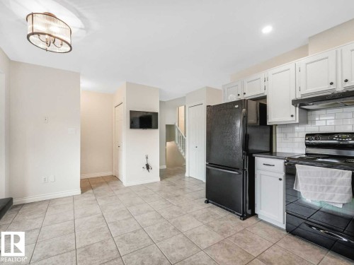 Kitchen area featuring tile flooring, white cabinetry, a subway tile backsplash, and a black range with an overhead exhaust hood - 4011 104 Street, Edmonton, AB - Indoor Photo Showing Kitchen