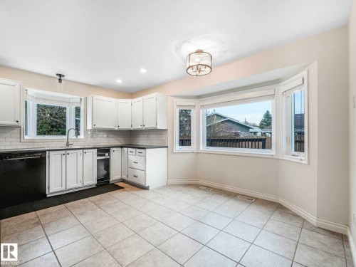 Kitchen area featuring white cabinetry, subway tile backsplash, dark countertops, and a bay window - 4011 104 Street, Edmonton, AB - Indoor Photo Showing Kitchen
